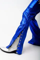 Pantalón azul metalizado de tiro alto, corte acampanado y aberturas laterales con botones dorados en los tobillos.