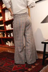 Pantalon de vestir de corte ancho y tiro alto, con cintura elástica fruncida. Presenta un diseño de estampado a cuadros en tonos grises y líneas finas en color naranja.