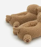 Pantufla cerrada de diseño divertido con forma de perro, confeccionada en tejido de poliéster tipo peluche color tostado, con detalles bordados de huellas en las patas.