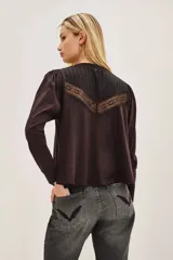 Camisa de manga larga color negro, con cuello redondo y cierre frontal de botones. Presenta un diseño con volados en la parte superior delantera y detalles de encaje bordado en los hombros y pecho.