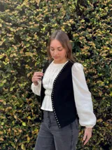Chaleco de cuero negro con tachas metálicas doradas en los bordes frontales.
