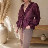 Blusa de tela semitransparente color bordó, con escote en V, volados decorativos en el frente, lazo para anudar y mangas largas amplias con puños ajustados.