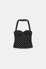 Top estilo corset con cuello halter y escote corazón, confeccionado en tela negra con estampado de lunares blancos. Presenta detalle de frunces en el delantero y cierre lateral oculto.