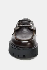 Mocasín de cuero marrón con diseño tipo náutico, presenta ojales metálicos laterales con cordones y suela de plataforma dentada en color negro.