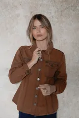 Chaqueta de denim color marrón, con corte entallado en la cintura, cierre frontal con botones metálicos y bolsillos superiores con solapa.