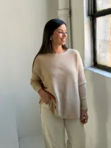 Sweater de punto en color beige, con cuello redondo, mangas largas con puños ajustados y diseño holgado con aberturas laterales en el ruedo.