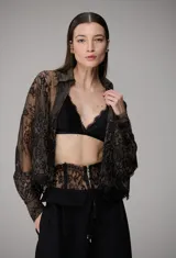Camisa de encaje negro con diseño semitransparente, cuello camisero, mangas largas y cierre frontal de botones.