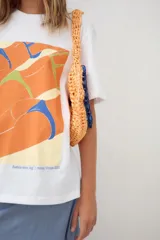 Remerón oversize de algodón blanco con estampado frontal de dos mujeres en bikini, con texto "Muertas de calor, cu pa arriba. Amiga hacerme un lugar. Desátame la bikini. Me quedo la marca? Pásame el Hawaiian. Eterno enero."