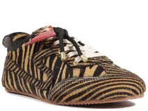 Sneaker de perfil bajo Schutz con estampado animal print tipo cebra en textura de pelo. Presenta cordones negros y blancos, con un detalle de parche triangular en color rojo en la lengüeta y suela plana de goma.