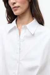 Camisa blanca de corte oversized, confeccionada en algodón, con cuello clásico, cierre frontal de botones y mangas cortas con vuelta.