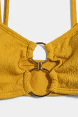 Top de bikini amarillo con textura sutil y detalle de aros metálicos entrelazados en el centro del escote, con tirantes finos.