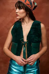 Chaleco de cuero y corderito color verde oscuro, sin mangas, con bolsillos delanteros y cierre mediante tiras de cuero para atar en el frente.