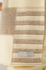 Bufanda de lana natural con diseño patchwork en tonos crema y beige, presentando bloques lisos y bloques con rayas horizontales.