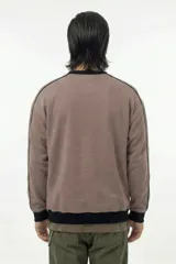 Buzo de cuello redondo en color marrón topo, con diseño de corte relajado. Presenta detalles de piping negro que recorren los hombros y las mangas, además de puños, cuello y cintura en tejido rib negro. Incluye el logo de la marca estampado en el pecho.