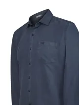Camisa de manga larga para hombre, color azul oscuro con efecto lavado/desgastado (ombre blue). Presenta cuello camisero, cierre frontal de botones y un bolsillo de parche en el pecho con un pequeño logo bordado.