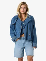 Trench corta de denim azul claro, con cuello solapa estilo biker, doble botonadura frontal y diseño holgado.