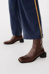 Bota corta de cuero color bordó, con punta cuadrada y taco bloque bajo. Cierre lateral con cremallera.