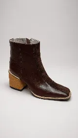 Botin de cuero y gamuza color marrón, con diseño combinado de paneles lisos y gamuzados, puntera cuadrada y taco bloque de madera con diseño geométrico. Cuenta con cierre lateral interno.