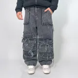 Pantalón jean de corte ultra baggy, color negro con efecto lavado. Presenta un diseño cargo con múltiples bolsillos laterales con bordes desflecados y detalles de costuras expuestas.