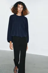Top azul marino de tejido fluido con cuello redondo y manga larga abullonada con aberturas. Presenta una abertura en la espalda con tira del mismo tejido y cierre de ganchos metálicos.