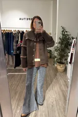 Campera de tela bouclé color marrón, con diseño de volados en tela agamuzada en el pecho y mangas. Presenta cierre frontal con botones y cuello redondo.
