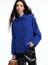 Camisa oversize de lyocell color tostado, con cuello clásico, cierre frontal de botones y mangas largas con puños anchos. Presenta un diseño de corte relajado con caída fluida.