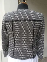 Chaqueta combinada en negro liso con tela estampada en blanco y negro, con vivos blancos, cierres en las mangas y bolsillos. Se prende con broches.
