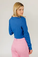 Top corto azul de tejido de punto acanalado, con mangas largas y cierre frontal con hebilla.