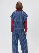 Campera de denim a rayas verticales con cuello de pana en color bordó. Presenta cierre frontal, mangas desmontables con cierre en los hombros, canesú en el pecho y bolsillos de parche cuadrados.