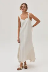 Vestido largo color crema, con breteles anchos y escote recto. Presenta corte irregular en el ruedo y volado en el bajo.