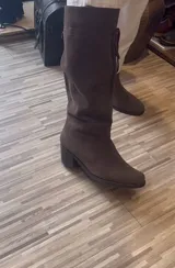 Bota de caña alta color suela, confeccionada en cuero napa, con diseño de caña caída y ajuste mediante cordones en la parte superior. Presenta un taco cuadrado foliado de 4,5 cm y suela de goma antideslizante.