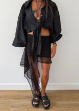 Falda corta negra de encaje con diseño irregular y un volante largo asimétrico en un lateral. Posee cintura elástica y forro interior.