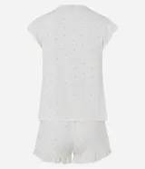 Pijama corto de dos piezas en color blanco con estampado continuo de pequeños corazones rosados. Incluye una blusa con escote en V, mangas cortas con volados, lazo frontal bajo el busto y un short con cintura elastizada y volados en los bajos.