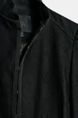 Chaqueta negra de cuello redondo, manga larga con hombreras abullonadas y cierre frontal con ganchos metálicos.