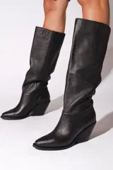 Bota de caña alta color negro, confeccionada en cuero vacuno. Tiene punta fina, taco de 6.5cm y suela de caucho antideslizante.