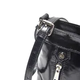 Bandolera de cuero negro con acabado brillante. Presenta dos bolsillos frontales con cierre metálico, herrajes plateados y placa metálica con logo en el centro. Incluye correa ajustable.