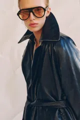 Trench oversize de efecto piel color azul marino, con cuello solapa, manga larga, bolsillos delanteros y cinturón ajustable del mismo tejido. Cierre frontal cruzado con botones y forro interior.