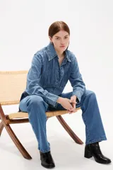 Camisa de jean con diseño de frunces verticales en el frente, cuello clásico, cierre frontal con botones y mangas largas con puños abotonados.