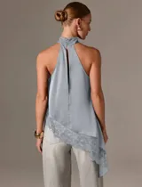 Blusa de satén color gris con cuello halter alto y fruncido, diseño sin mangas, corte asimétrico y detalle de encaje en el borde inferior.
