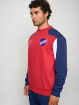 Buzo de felpa con diseño de bloques de color, predominantemente rojo en el cuerpo y azul marino en las mangas y hombros. Presenta el escudo del Club Nacional de Football y el logo de Umbro en el pecho.