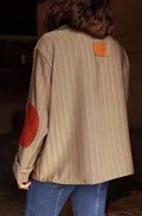 Blazer de corte oversize confeccionado en tela casimir a rayas, con cuello tipo lazo y parches de cuero en los codos y bolsillos frontales.