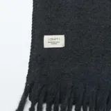 Bufanda de tejido suave en color negro, con diseño de flecos en los extremos.