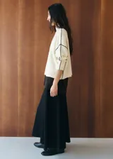 Chaleco de punto color blanco con detalles de líneas negras en los hombros y sisas, cuello alto y diseño holgado.
