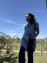 Camisa tipo vestido a rayas celestes, rojas y blancas, con cuello alto fruncido, mangas cortas abullonadas con puños elásticos y cierre frontal de botones.