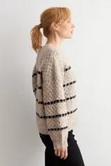 Sweater de punto con textura, color beige melange con rayas horizontales negras. Presenta cuello redondo, mangas largas y corte holgado.
