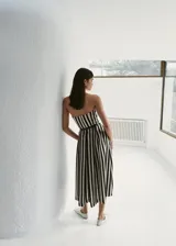 Vestido midi de corte evasé con diseño de rayas verticales en blanco y negro, escote palabra de honor y detalle de cinturón fino en la cintura.