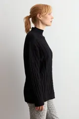 Polerón de punto negro con cuello alto y diseño de trenzas verticales en el frente. Posee mangas largas con puños acanalados y un corte holgado.