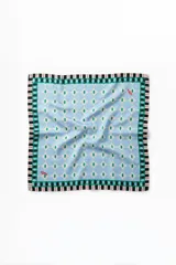 Pañuelo cuadrado de seda con estampado geométrico de círculos celestes y puntos verdes sobre fondo claro. Presenta un borde decorativo con rombos verdes y una franja perimetral a rayas blancas, negras y rojas.