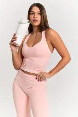 Conjunto deportivo de dos piezas en color rosa pastel. Incluye un top de escote redondo con espalda estilo nadadora y logo estampado en el frente, y una calza de tiro alto con costuras reforzadas a tono.