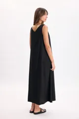 Vestido largo negro sin mangas, con escote en V, pinzas frontales, bolsillos laterales y caída fluida.